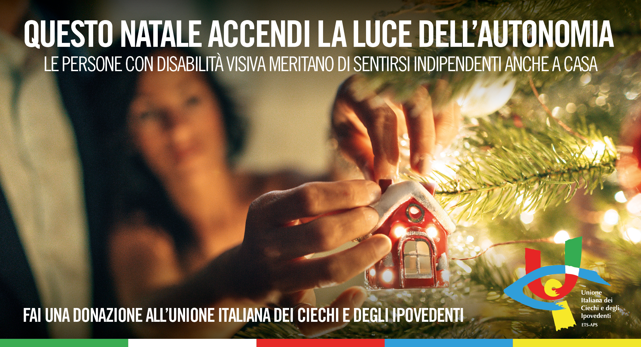 Nellimmagine c una figura maschile, appena intuibile nello sfondo sfocato, accanto a una donna illuminata da una luce calda e morbida tipica dellatmosfera natalizia. In primo piano, le mani di lei appendono una piccola decorazione a forma di casetta rossa su un ramo dellalbero di Natale. La scena trasmette attenzione e la magia discreta di un gesto semplice ma pieno di significato. In alto la scritta: Questo Natale accendi la luce dell'autonomia. Le persone con disabilit visiva meritano di sentirsi indipendenti anche a casa; in basso: Fai una donazione all'Unione Italiana dei Ciechi e degli Ipovedenti accanto al logo UICI.